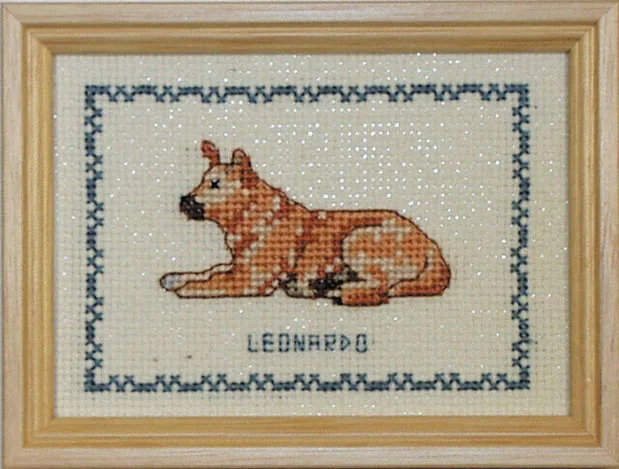 Broderikit fra Permin med en liggende hund i varme rødbrune og gyldne nuancer broderet i korssting og navnet LEONARDO