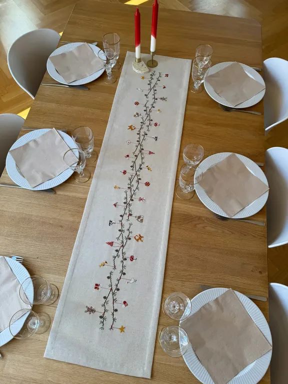 Juleløberen Julestemning på et lyst træbord med tallerkener, glas og røde stearinlys
