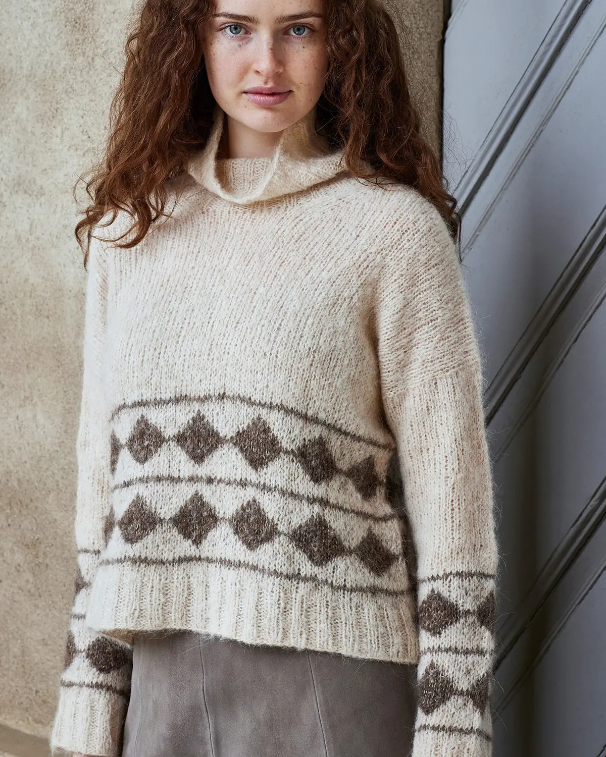 Kvinde i cremefarvet sweater med brunt mønsterstrik forneden og på ærmerne, strikket i Nanna by Permin
